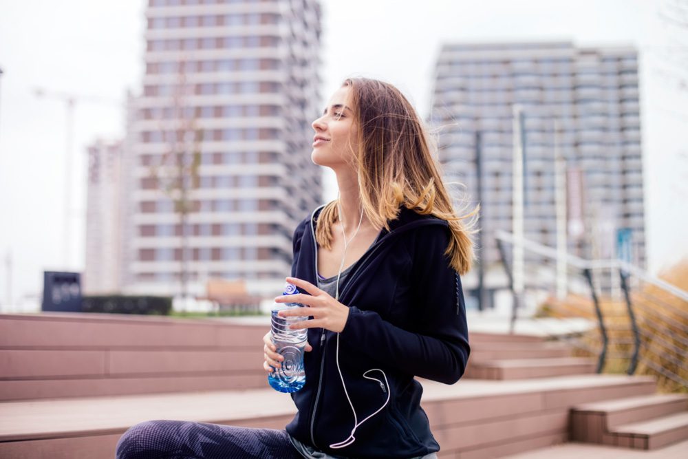 A young woman is exercising and hydrating outside, leading a healthy lifestyle to assist in successful TMS therapy.
